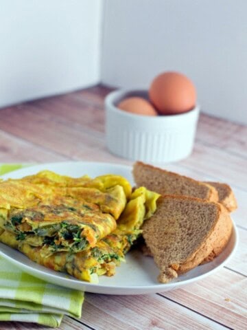 Indian omelette served in a white plate with brown bread slices