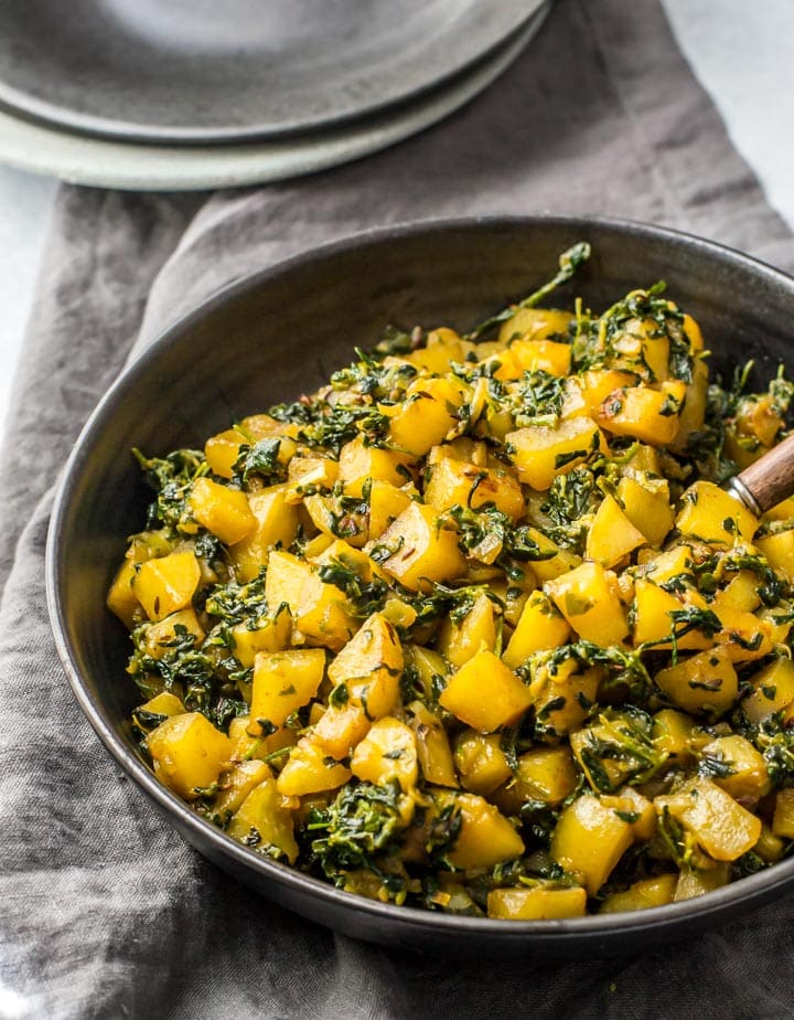 Aloo methi served in a black bowl along with a grey napkin