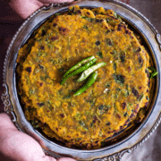 Methi thepla served on a metal plate with green chilies on top