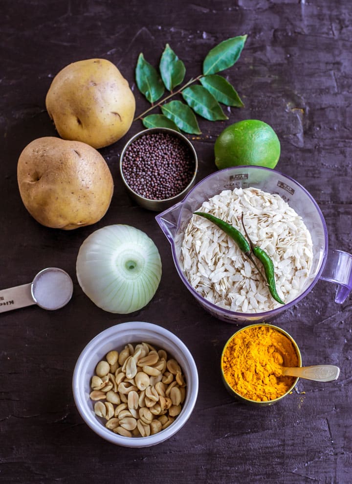 Shows ingredients for Poha - curry leaves, potatoes, mustard seeds, onions, salt, peanuts, turmeric powder, lemon, green chilies and poha