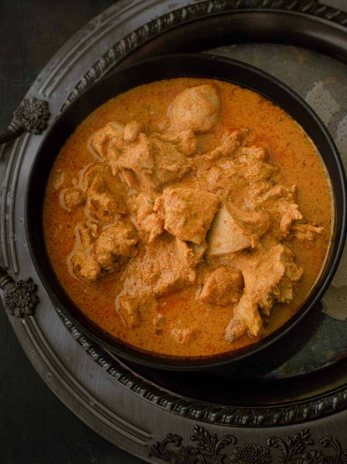 Mangalorean chicken curry or Kori Gassi is served in a black bowl with crispy rice wafers on the side.