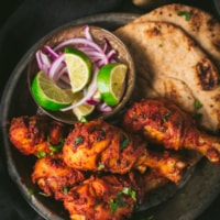Tandoori chicken is served with a side of lemon wedges, sliced onions and naan