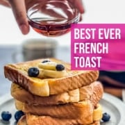 A blue plate with a tall stack of french toast and some blueberries to garnish. A hand holding a bowl of syrup and the words best ever french toast at the top of the picture.