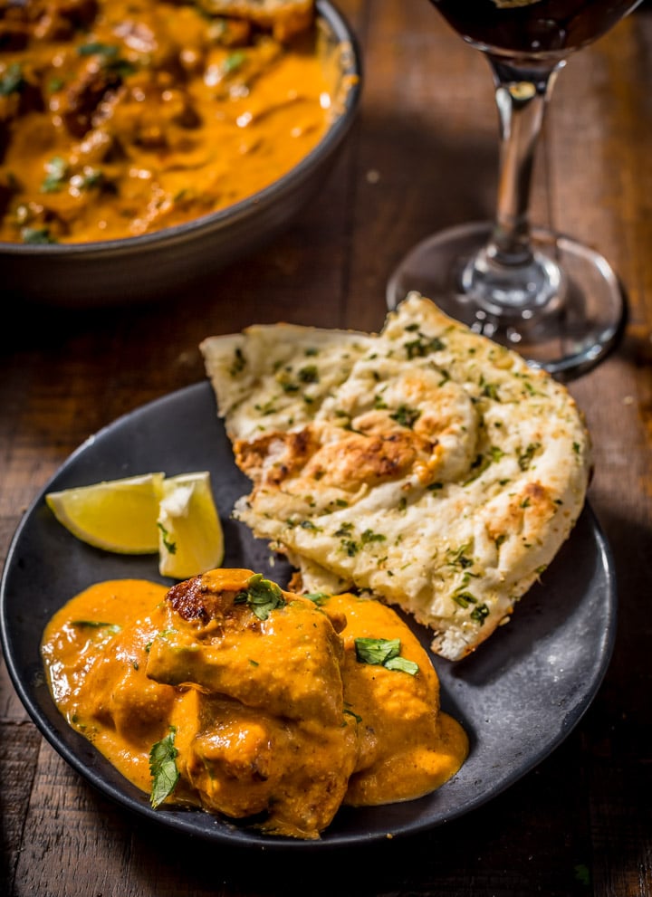 An overhead shot of chicken tikka masala served in a black plate with garlic naan