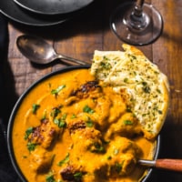Chicken Tikka Masala served in a black bowl with garlic naan dipped in it