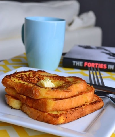 A stack of French toast placed on a white plate with coffee on the side