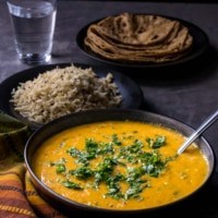 dal served in a black bowl with rice, roti and water on the side