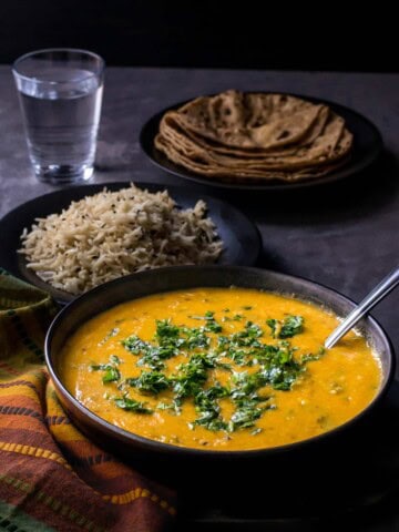 dal served in a black bowl with rice, roti and water on the side