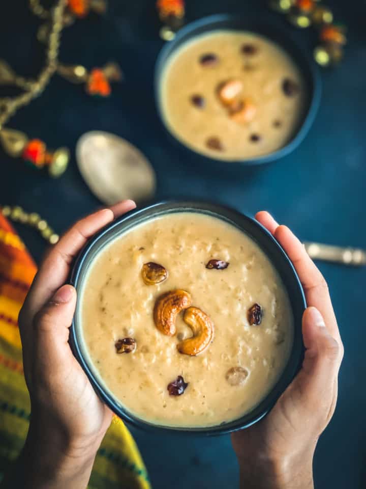A hand holding a bowl of moong dal payasam served in a black bowl