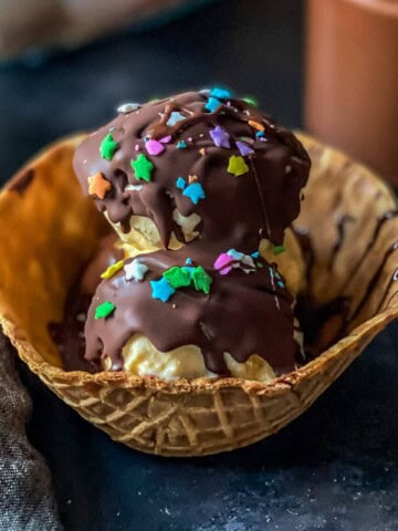 A waffle bowl with scoops of vanilla ice cream topped with homemade magic shell and sprinkles.