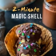 The words 2 minute magic shell in the top of the photo with a waffle cone bowl with vanilla ice cream topped with magic shell sauce and sprinkles on a dark counter.