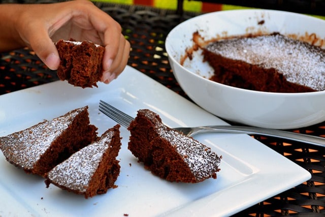 A hand holding a piece of cake. Chocolate cake  pieces served on a white plate. 