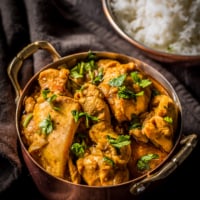 An overheat shot of chicken chettinad served in a copper coated bowl. Accompanied by rice.