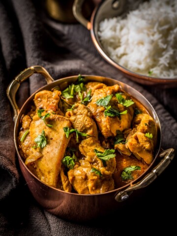 An overheat shot of chicken chettinad served in a copper coated bowl. Accompanied by rice.