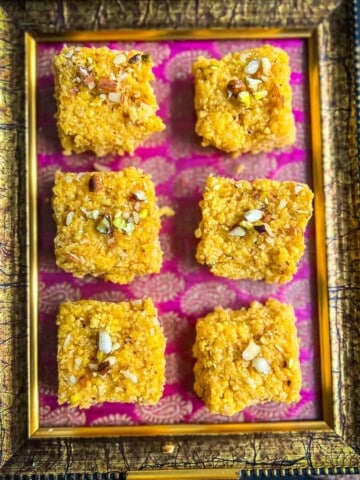 6 pieces of mango kalakand placed on a pink and golden tray