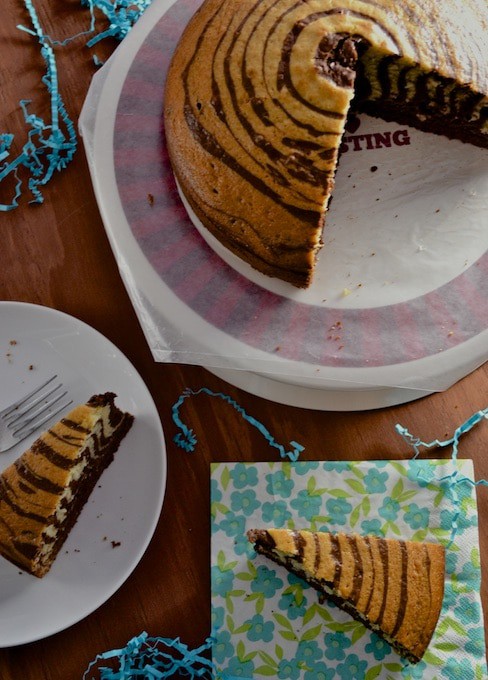 Zebra cake on a cake stand with a white plate with a slice of cake on the side.