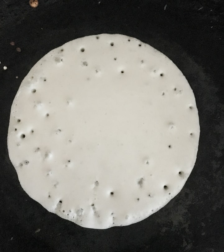 Kappa rotti cooking in a pan. Bubbles are formed on top of this dosa indicating the consistency is right