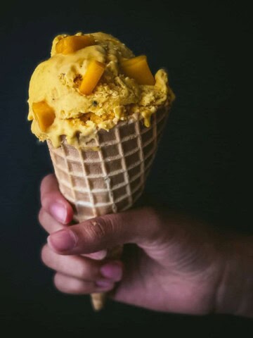 A hand holding a cone filled with mango ice cream