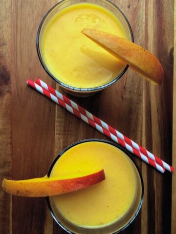 Mango Milkshake served in two glasses with 2 straws placed in between the two glasses
