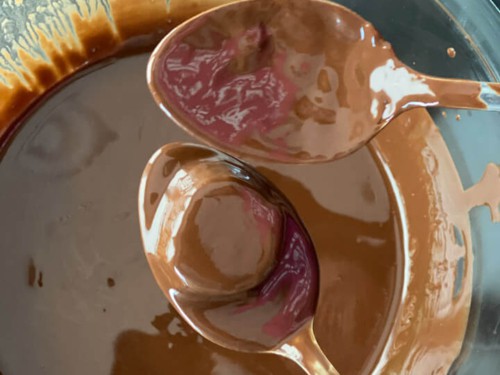 Banana bite covered with chocolate placed on a spoon over a glass bowl of chocolate