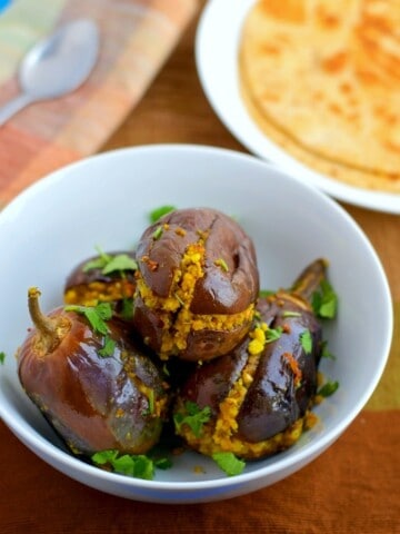 An overhead shot of stuffed brinjal (bharva bhaingan) served in a white bowl alongside rotis