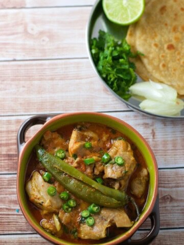 Achari chicken served in a green bowl with a side of rotis