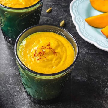 Two glasses of Mango lassi served with a plate of mango slices