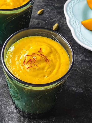 Two glasses of Mango lassi served with a plate of mango slices