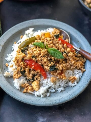 A light blue plate topped with fresh rice covered in thai basil chicken and a fork to the right.