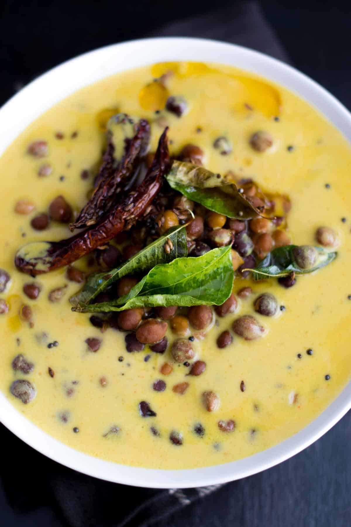 Kaale channe ki kadhi served in a white bowl with tempering of red chilies and curry leaves on top