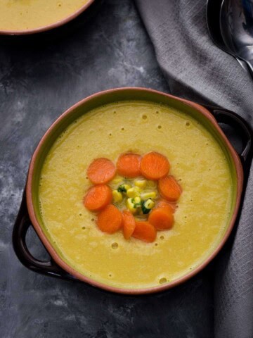 Indo chinese corn soup topped with chopped carrots and served in a green and black bowl