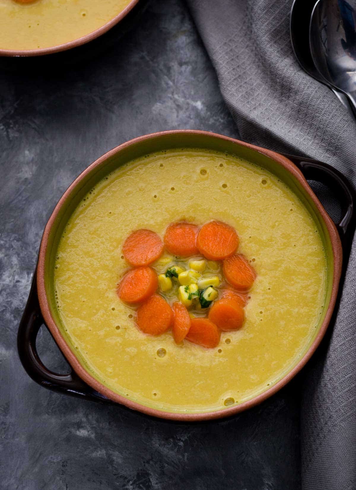 Indo chinese corn soup topped with chopped carrots and served in a green and black bowl