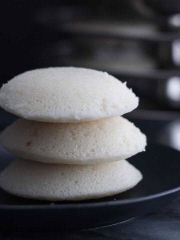 Three idlis stacked in a black plate
