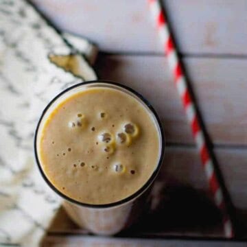 Date and Chikoo Smoothie served in a glass with a red and white straw on the side