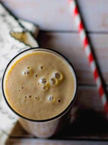 Date and Chikoo Smoothie served in a glass with a red and white straw on the side