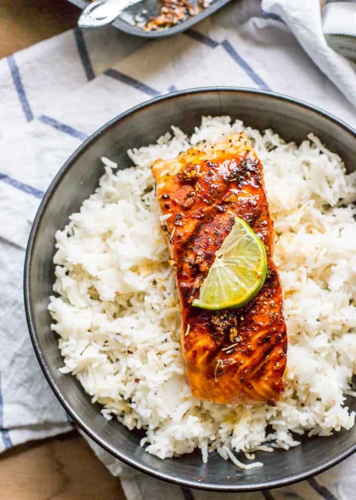 Honey garlic salmon with a lime slice on top served over a bed of rice in a black bowl