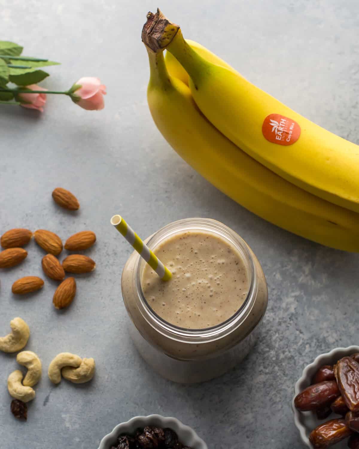 Overhead shot of a mason jar with smoothie with banana, cashews, raisins and dates on the side