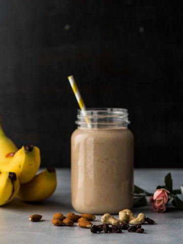 A mason jar with smoothie with banana, cashews, raisins and dates on the side