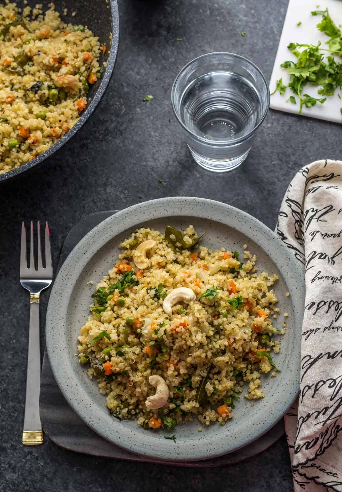Vegetable Quinoa Pulao garnished with cashews on a grey plate with fork on the side.