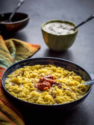 Khichdi served in a black bowl with pickle on top and served with raita