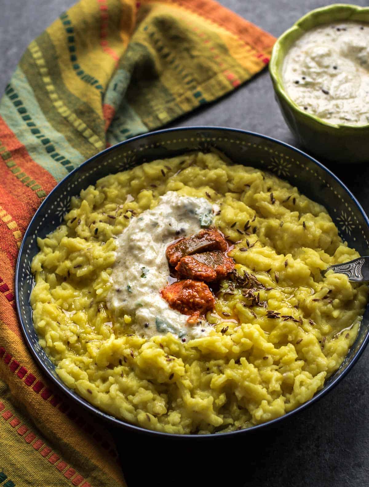 Moong dal khichdi served with raita and pickle in a blue bowl