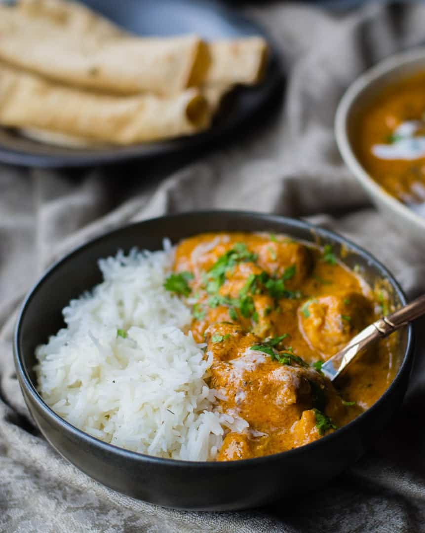 Chicken makhani served in a black bowl with rice and served with roti