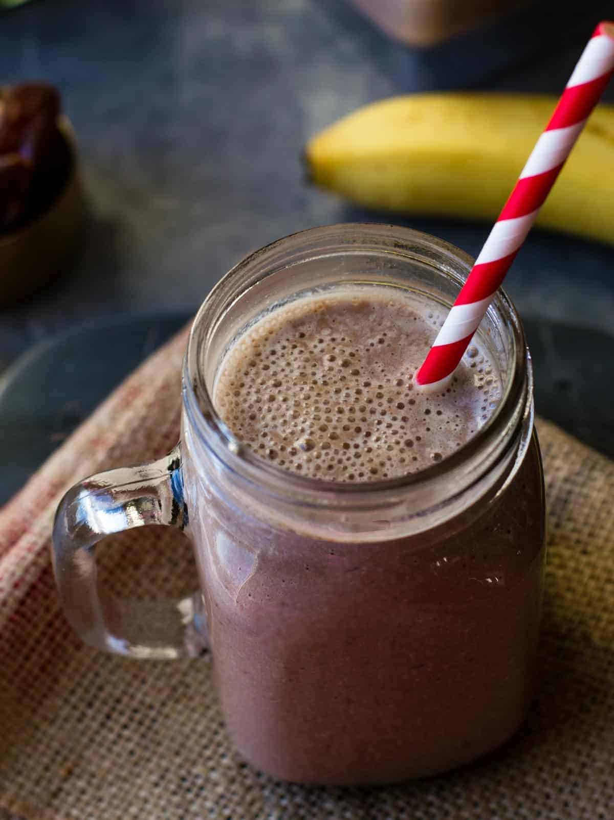 Chocolate almond smoothie served in a glass jar with a red and white straw