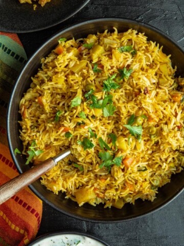 An overhead shot of Instant Pot Vegetable Biryani in a black bowl accompanied by a orange and green napkin