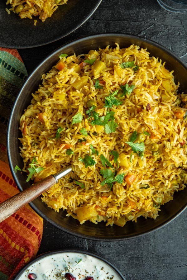 An overhead shot of Instant Pot Vegetable Biryani in a black bowl accompanied by a orange and green napkin