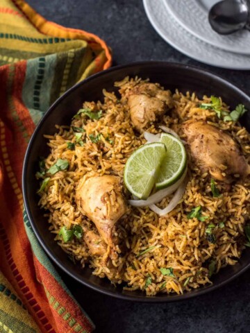 Chicken biryani served in a black bowl with lime wedges on top