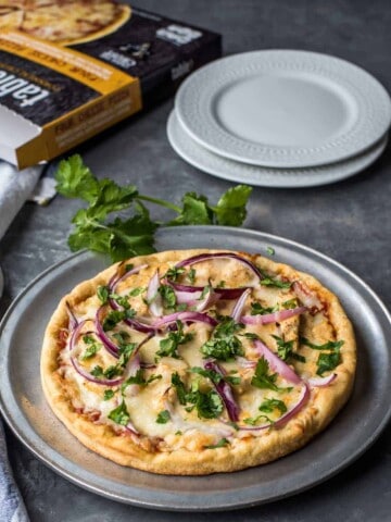 Chicken tikka masala pizza on a pewter plate with two white plates on the side