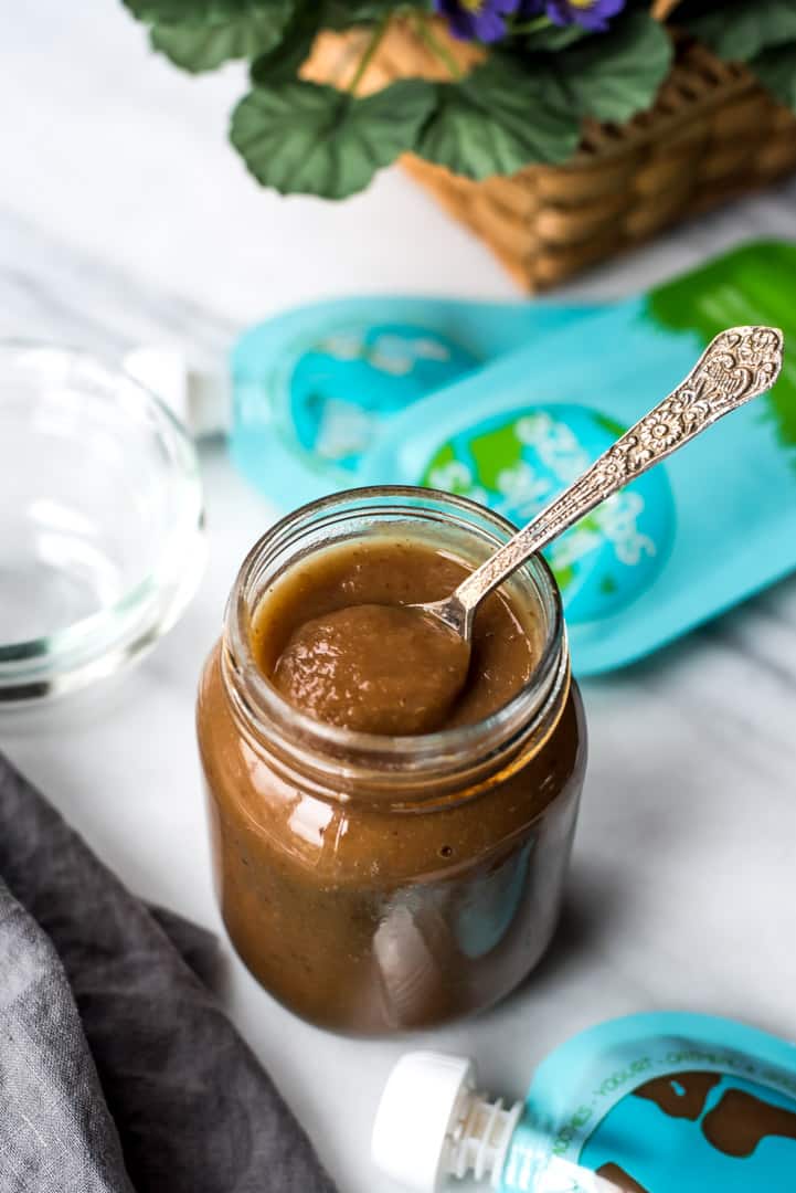 Instant Pot Applesauce served in a glass bottle along with a spoon. Reusable pouches are on the side.