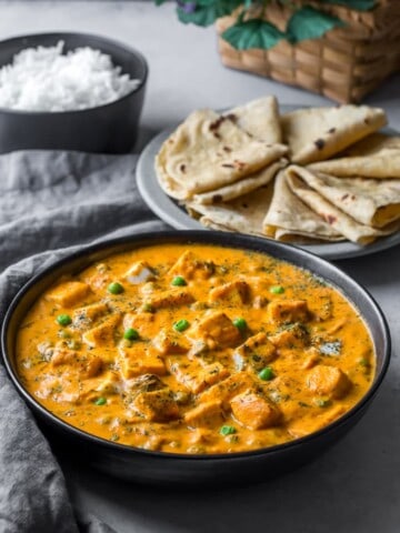 Matar paneer served in a black bowl alongside rotis