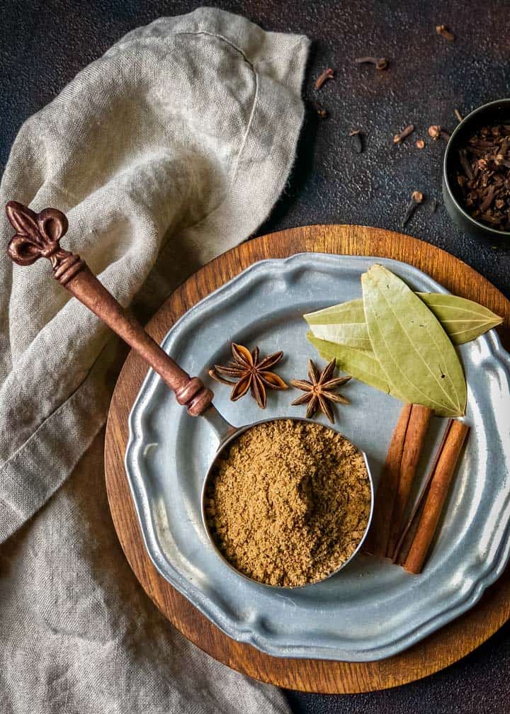 1/2 cup measuring cup filled with garam masala surrounded by whole spices